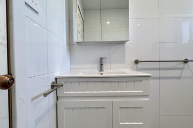 Small modern bathroom in Sydney with recessed-panel cabinets, white cabinets, a corner shower, a one-piece toilet, white tile, ceramic tile, white walls, porcelain floors, a drop-in sink, laminate benchtops, grey floor, a hinged shower door, white benchtops, a niche, a single vanity and a freestanding vanity.