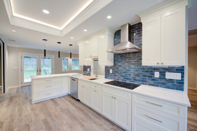 This is an example of a medium sized traditional galley kitchen/diner in New York with a submerged sink, shaker cabinets, white cabinets, composite countertops, blue splashback, metro tiled splashback, stainless steel appliances, medium hardwood flooring, a breakfast bar, beige floors and white worktops.