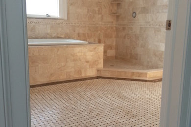 This is an example of an expansive traditional master bathroom in New York with a drop-in tub, an alcove shower, beige tile, stone tile, beige walls and marble floors.