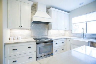 Mid-sized transitional l-shaped porcelain tile kitchen photo in Phoenix with a farmhouse sink, shaker cabinets, white cabinets, quartzite countertops, gray backsplash, porcelain backsplash, stainless steel appliances and an island