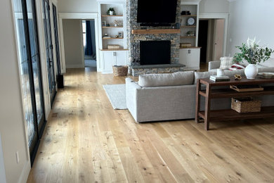 Cette image montre un grand salon design ouvert avec un mur blanc, un sol en bois brun, une cheminée standard, un manteau de cheminée en pierre, un sol marron et poutres apparentes.