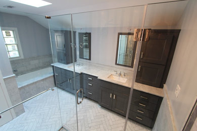 Example of a mid-sized transitional master gray tile and porcelain tile marble floor and white floor corner shower design in DC Metro with recessed-panel cabinets, black cabinets, an undermount tub, gray walls, an undermount sink, marble countertops and a hinged shower door