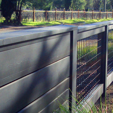 Visually quiet black stained board fence transitions to open hogwire fence