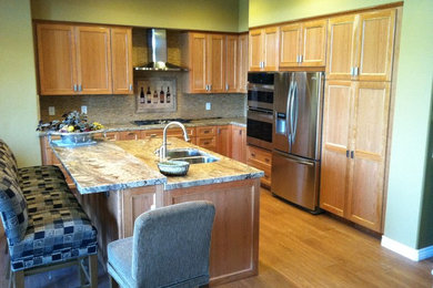 Large transitional l-shaped light wood floor enclosed kitchen photo in Los Angeles with a double-bowl sink, shaker cabinets, light wood cabinets, granite countertops, beige backsplash, stone tile backsplash, stainless steel appliances and an island