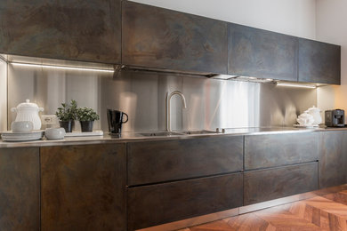 Mid-sized contemporary single-wall eat-in kitchen in Milan with flat-panel cabinets, metallic splashback, stainless steel cabinets and stainless steel benchtops.
