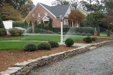 This is an example of a large contemporary full sun front yard stone retaining wall landscape in Raleigh.