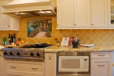 This is an example of a mid-sized traditional galley kitchen in Orange County with recessed-panel cabinets, white cabinets, granite benchtops, yellow splashback, ceramic splashback, stainless steel appliances, an undermount sink, dark hardwood floors, brown floor and multi-coloured benchtop.
