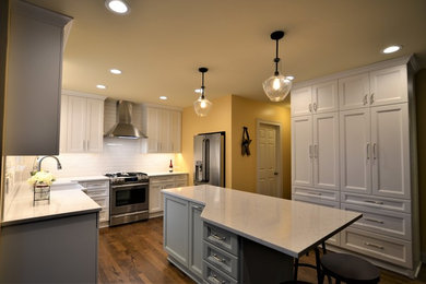 Inspiration for a mid-sized transitional l-shaped medium tone wood floor and brown floor enclosed kitchen remodel in Chicago with a farmhouse sink, shaker cabinets, white cabinets, quartz countertops, white backsplash, subway tile backsplash, stainless steel appliances and an island