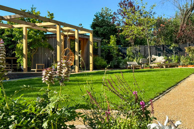Large contemporary back formal partial sun pergola for summer in London with gravel and a wood fence.