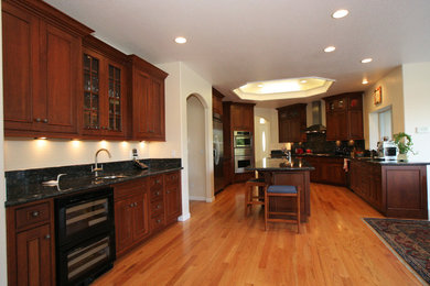 Large elegant u-shaped light wood floor eat-in kitchen photo in Sacramento with recessed-panel cabinets, medium tone wood cabinets, granite countertops, stone slab backsplash, stainless steel appliances and an island