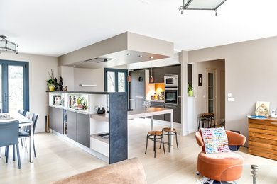 Aménagement d'une grande cuisine américaine moderne en L et bois brun avec un évier encastré, un placard à porte plane, un plan de travail en granite, une crédence orange, un électroménager en acier inoxydable, parquet clair, une péninsule, une crédence en bois, un sol beige et un plan de travail gris.