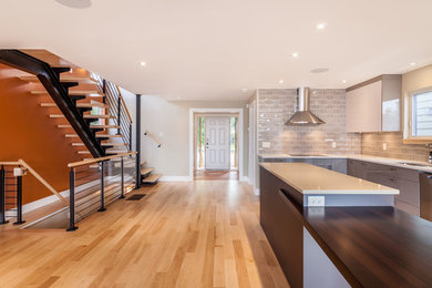 Inspiration for a mid-sized contemporary l-shaped light wood floor eat-in kitchen remodel in Other with a double-bowl sink, flat-panel cabinets, gray cabinets, solid surface countertops, gray backsplash, subway tile backsplash, stainless steel appliances and an island