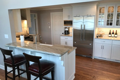 Example of a mid-sized transitional medium tone wood floor kitchen design in Charlotte with a farmhouse sink, shaker cabinets, white cabinets, white backsplash, stainless steel appliances, a peninsula and quartzite countertops