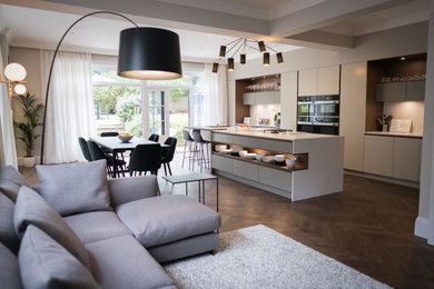Design ideas for a large transitional l-shaped open plan kitchen in Hertfordshire with a drop-in sink, flat-panel cabinets, grey cabinets, solid surface benchtops, white splashback, panelled appliances, dark hardwood floors, with island, brown floor and white benchtop.