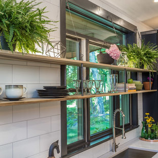 Large industrial kitchen pantry photos - Inspiration for a large industrial l-shaped cement tile floor and gray floor kitchen pantry remodel in Milwaukee with an undermount sink, flat-panel cabinets, black cabinets, quartz countertops, white backsplash, porcelain backsplash, stainless steel appliances, an island and white countertops