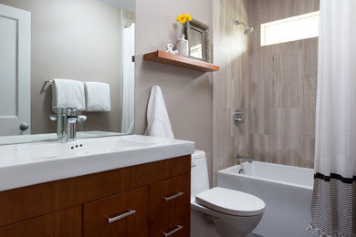 Example of a small trendy 3/4 beige tile and stone tile slate floor and gray floor bathroom design in San Francisco with flat-panel cabinets, medium tone wood cabinets, beige walls, a wall-mount sink, a one-piece toilet and solid surface countertops