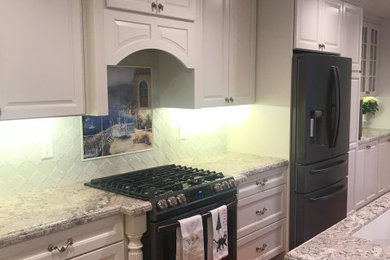 Enclosed kitchen - mid-sized mediterranean galley medium tone wood floor and brown floor enclosed kitchen idea in Orange County with an undermount sink, raised-panel cabinets, white cabinets, granite countertops, beige backsplash, granite backsplash, black appliances, an island and beige countertops