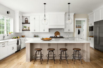 Inspiration for a transitional light wood floor kitchen remodel in DC Metro with a farmhouse sink, shaker cabinets, white cabinets, quartz countertops, white backsplash, ceramic backsplash, stainless steel appliances, an island and white countertops