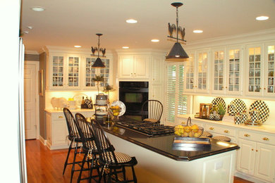 Mid-sized cottage single-wall medium tone wood floor eat-in kitchen photo in Other with glass-front cabinets, white cabinets, solid surface countertops, white backsplash, black appliances and an island