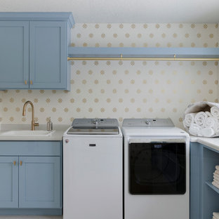 他の地域のトラディショナルスタイルのおしゃれな洗濯室 (ドロップインシンク、シェーカースタイル扉のキャビネット、青いキャビネット、ラミネートカウンター、左右配置の洗濯機・乾燥機、マルチカラーの壁、ベージュの床) の写真