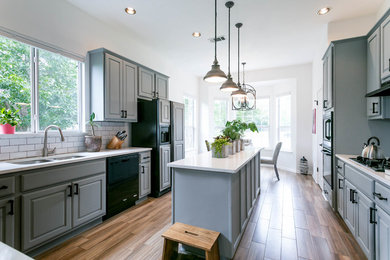 Transitional u-shaped porcelain tile and brown floor eat-in kitchen photo in Austin with a double-bowl sink, gray cabinets, quartz countertops, white backsplash, ceramic backsplash, black appliances and an island
