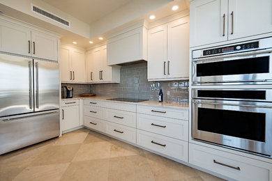 Large transitional l-shaped separate kitchen in Miami with a farmhouse sink, recessed-panel cabinets, white cabinets, granite benchtops, grey splashback, glass tile splashback, stainless steel appliances, travertine floors and with island.