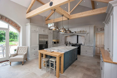 Photo of a large traditional l-shaped eat-in kitchen in Other with a farmhouse sink, shaker cabinets, white splashback, with island, beige floor, marble benchtops, stainless steel appliances and travertine floors.