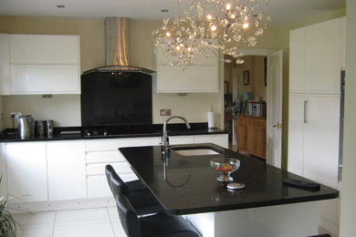 This is an example of a large modern u-shaped separate kitchen in Other with a drop-in sink, flat-panel cabinets, granite benchtops, black splashback, glass sheet splashback, stainless steel appliances, ceramic floors and with island.