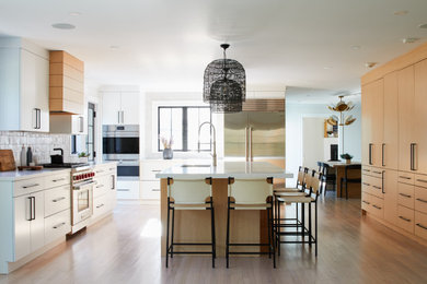Inspiration for an expansive contemporary u-shaped open plan kitchen in New York with an undermount sink, flat-panel cabinets, quartz benchtops, grey splashback, ceramic splashback, stainless steel appliances, light hardwood floors, with island, beige floor, white benchtop and medium wood cabinets.