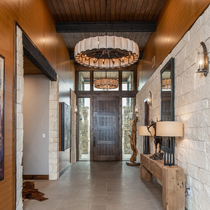 Example of a large mountain style limestone floor, gray floor, exposed beam and wall paneling entryway design in Austin with multicolored walls and a dark wood front door