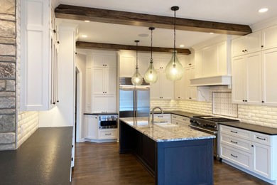 Photo of a large transitional u-shaped kitchen in Milwaukee with a farmhouse sink, recessed-panel cabinets, white cabinets, granite benchtops, multi-coloured splashback, stainless steel appliances, dark hardwood floors, with island, brown floor and black benchtop.