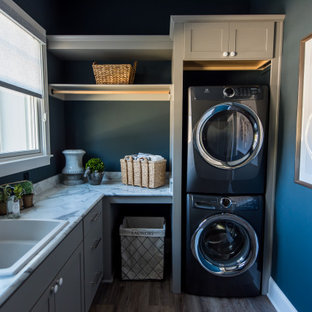 Photo of a medium sized classic l-shaped separated utility room in Indianapolis with a built-in sink, shaker cabinets, grey cabinets, blue walls, medium hardwood flooring, a stacked washer and dryer, brown floors and grey worktops.