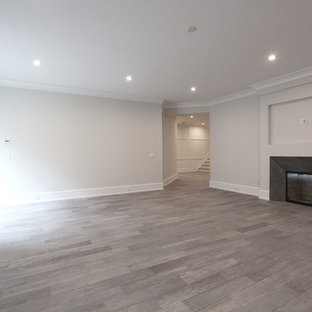 ニューヨークの大きいビーチスタイルのおしゃれな地下室 (半地下 (ドアあり)、グレーの壁、無垢フローリング、標準型暖炉、金属の暖炉まわり、茶色い床) の写真