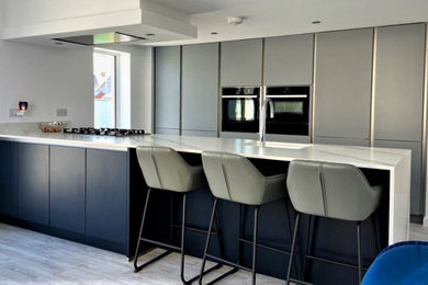 Photo of a medium sized modern single-wall kitchen/diner in Other with a submerged sink, flat-panel cabinets, grey cabinets, quartz worktops, black appliances, light hardwood flooring, an island, grey floors and white worktops.