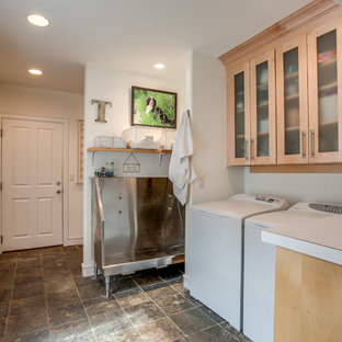 This is an example of a country single-wall utility room in Seattle with an utility sink, glass-front cabinets, light wood cabinets, white walls and a side by side washer and dryer.