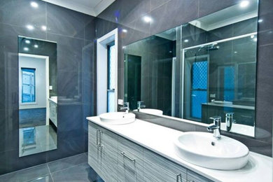 This is an example of a modern bathroom in Brisbane with grey cabinets, granite benchtops, a freestanding tub, a double shower, gray tile, porcelain tile, grey walls and porcelain floors.