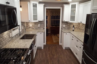 Mid-sized farmhouse galley dark wood floor and brown floor enclosed kitchen photo in Miami with a farmhouse sink, shaker cabinets, white cabinets, quartz countertops, brown backsplash, stone tile backsplash, black appliances, no island and beige countertops