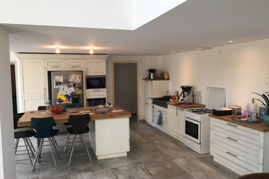 This is an example of an expansive traditional single-wall kitchen/diner in Angers with a built-in sink, shaker cabinets, white cabinets, wood worktops, stainless steel appliances, ceramic flooring, an island and grey floors.