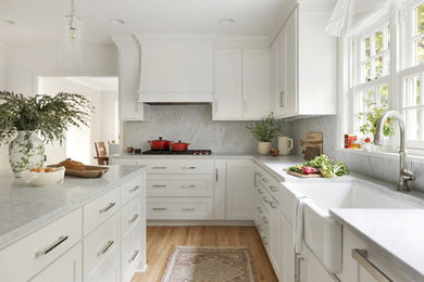 Example of a classic limestone floor kitchen design in Minneapolis with a farmhouse sink, white cabinets, gray backsplash, an island and gray countertops