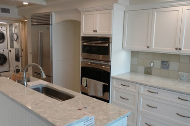 Eat-in kitchen - large transitional eat-in kitchen idea in Tampa with an undermount sink, recessed-panel cabinets, white cabinets, beige backsplash, ceramic backsplash, stainless steel appliances and an island