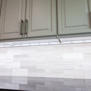 Cette photo montre une grande arrière-cuisine parallèle chic avec un évier encastré, un placard avec porte à panneau surélevé, des portes de placard blanches, un plan de travail en quartz, une crédence multicolore, une crédence en pierre calcaire, un électroménager en acier inoxydable, un sol en bois brun, un îlot central et un sol marron.