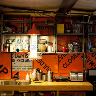 Новый формат декора квартиры: маленькая параллельная кухня в стиле лофт с обеденным столом, врезной раковиной, открытыми фасадами, светлыми деревянными фасадами, столешницей из дерева, оранжевым фартуком, фартуком из металлической плитки, техникой из нержавеющей стали и полом из фанеры без острова