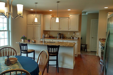 Inspiration for a mid-sized timeless single-wall medium tone wood floor eat-in kitchen remodel in Other with an undermount sink, raised-panel cabinets, distressed cabinets, granite countertops, stainless steel appliances and an island