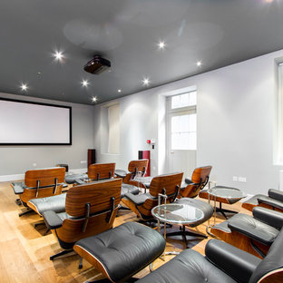 This is an example of a contemporary enclosed home cinema in London with white walls, light hardwood flooring, a projector screen and yellow floors.