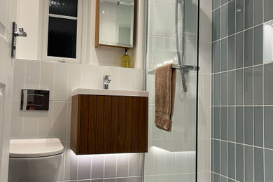 This is an example of a small modern bathroom in Gloucestershire with medium wood cabinets, a walk-in shower, a wall mounted toilet, blue tiles, ceramic tiles, white walls, an integrated sink, an open shower, white worktops, a wall niche, a single sink and a floating vanity unit.