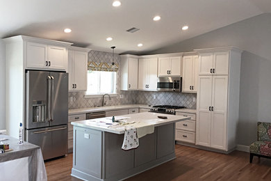 Mid-sized trendy u-shaped laminate floor and beige floor eat-in kitchen photo in Los Angeles with a single-bowl sink, flat-panel cabinets, white cabinets, granite countertops, gray backsplash, ceramic backsplash, stainless steel appliances, an island and white countertops