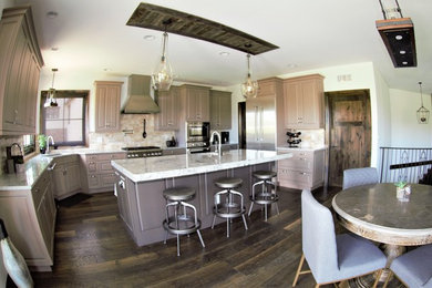 This is an example of a large country u-shaped open plan kitchen in Denver with a drop-in sink, shaker cabinets, grey cabinets, granite benchtops, beige splashback, porcelain splashback, stainless steel appliances, dark hardwood floors, with island, brown floor and grey benchtop.