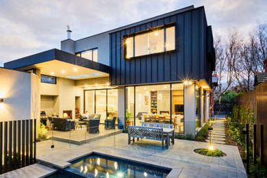 Photo of a modern two-storey black house exterior in Melbourne with metal siding, a flat roof and a metal roof.
