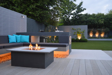Photo of a large contemporary backyard partial sun garden in London with a fire feature and decking.
