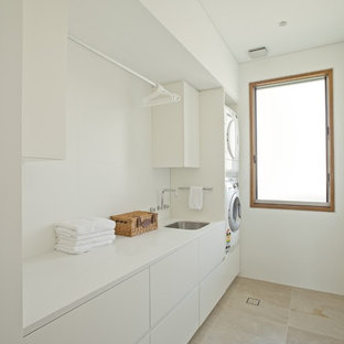 シドニーの大きいコンテンポラリースタイルのおしゃれな洗濯室 (シングルシンク、フラットパネル扉のキャビネット、白いキャビネット、テラゾーカウンター、白い壁、ライムストーンの床、上下配置の洗濯機・乾燥機、ベージュの床、白いキッチンカウンター) の写真